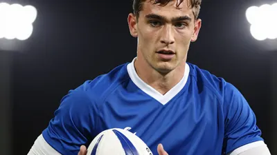 A 23-year-old full-back in a blue shirt with white sleeves, playing with a white ball at his feet, in a tight action...