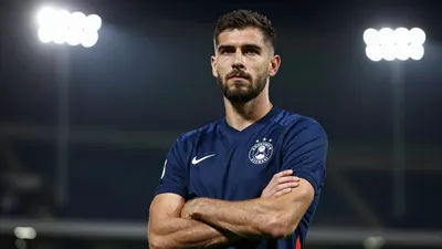 A 33-year-old centre-back in a solid navy blue kit, standing confidently with arms crossed