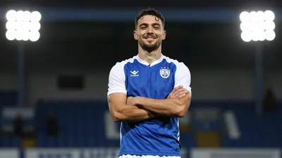 A photorealistic image of an anonymous FC Halifax Town player, aged 25-30, wearing a blue jersey with white sleeves and a...