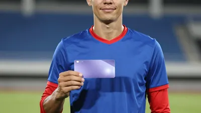 Mid-20s male player, athletic build, waist-up, wearing a plain blue shirt with red sleeves and collar, unmarked fabric...
