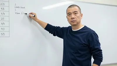 A 40-year-old, clean-shaven, anonymous coach with a stern expression, wearing a dark blue, long-sleeved, cotton shirt...