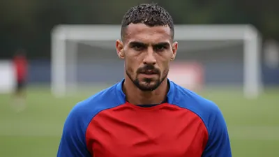 Mid-30s muscular forward, head-and-shoulders, intense gaze, wearing a plain blue and red training top (solid blue...