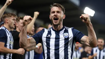 A mid-30s FC Halifax Town player in a navy blue and white striped shirt, celebrating with fans after scoring