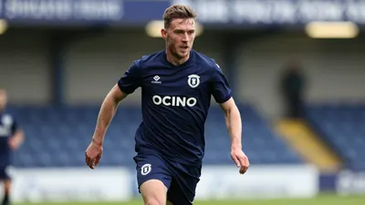 A focused FC Halifax Town midfielder, 25-30 years old, athletic build, in solid navy blue kit, driving forward with the...
