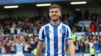 A 25-year-old FC Halifax Town midfielder in a blue and white striped kit, shot with a 50mm lens at f/2.8, with a slight...