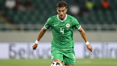 A dynamic shot of a midfielder in a green shirt, number 4, in action during a match, controlling the ball in midfield