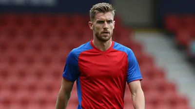 Mid-30s athletic midfielder, lean, determined expression, returning to training after injury, waist-up, wearing a plain...