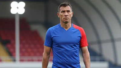 Middle-aged, lean coach, mid-30s, short dark hair, intense eyes, waist-up, wearing an unmarked training top split blue...