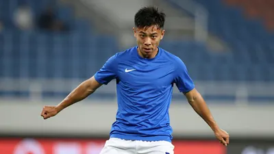 A young, athletic forward in his mid-20s, wearing a solid blue shirt and white shorts, captured waist-up as he prepares...