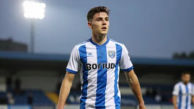 A 21-year-old striker in action, wearing FC Halifax Town's kit, with a floodlight rim light and shallow depth of field...