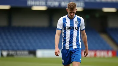 A tight waist-up shot of an anonymous FC Halifax Town player in his home kit, with a blue and white striped top and blue...