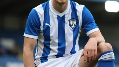 A photorealistic image of an anonymous FC Halifax Town player, aged 25-30, wearing a blue and white striped shirt, with a...